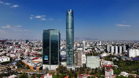 Aerial-view-away-from-the-Torre-Mitikah-tower,-in-sunny-Mexico-city---pull-back,-drone-shot