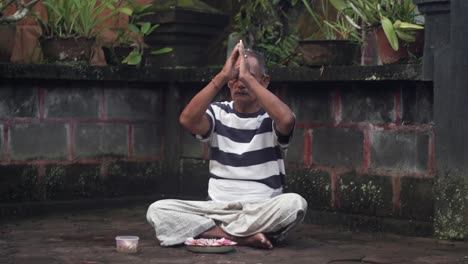 Porträt-Eines-Balinesischen-Mannes,-Der-Mit-Den-Händen-An-Der-Stirn-Betet-Und-Außerhalb-Des-Hinduistischen-Tempels-Sitzt