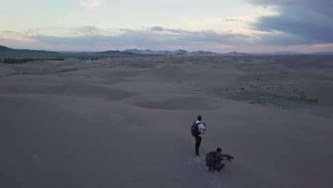 Two-photographers-at-top-of-dune-photograph-Mojave-Desert,-Utah-sunset