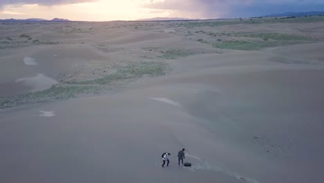 Two-photographers-climb-sand-dune-in-Mojave-Desert,-Utah-at-sunset