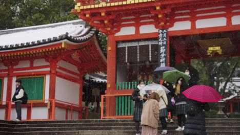 Snow-Falling-over-Yasaka-Jinja,-Tourists-Visit-Site-Holding-Umbrellas