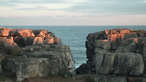 Gap-view-between-ocean-cliffs-or-rocks,-Cascais-coast-in-Portugal,-calm-steady-shot