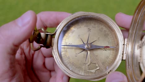 Close-up-shot-of-man-watching-retro-golden-compass-in-wilderness-at-sunny-day