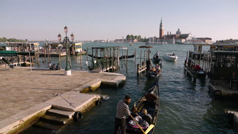 Gondolas-With-Tourists-Leaving-The-Pier-In-The-Embankment-Of-The-Grand-Canal-In-Venice,-Italy