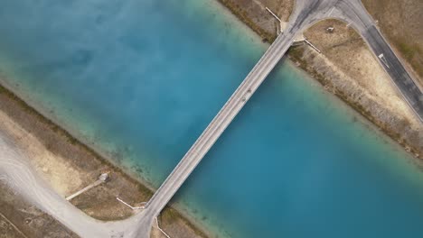 From-the-sky,-one-can-witness-the-grandeur-of-cyclists-crossing-the-Pukaki-Canals-by-a-bridge