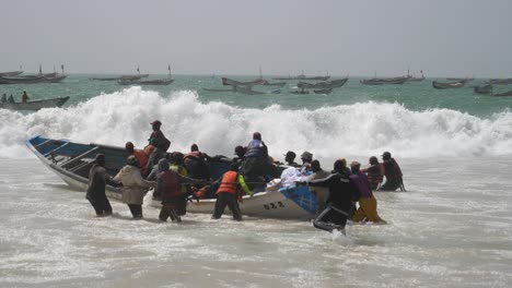 Gente-Tratando-De-Empujar-El-Barco-De-Pesca-Hacia-El-Mar-Agitado,-La-Playa-Y-La-Costa-De-Mauritania,-áfrica