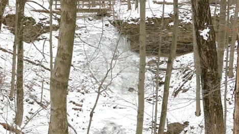 Frozen-waterfall-in-woods-in-winter-with-small-river-flow