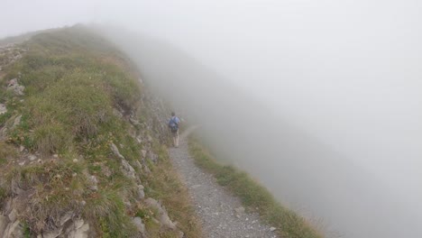 Man-hikes-alone,-walks-into-fog-on-narrow-mountain-trail-in-Swiss-Alps