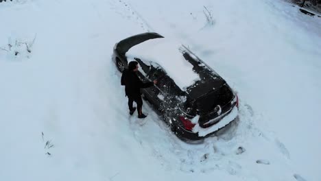 El-Hombre-Barre-La-Nieve-Del-Auto-Negro-Después-De-Fuertes-Nevadas,-Vista-Aérea