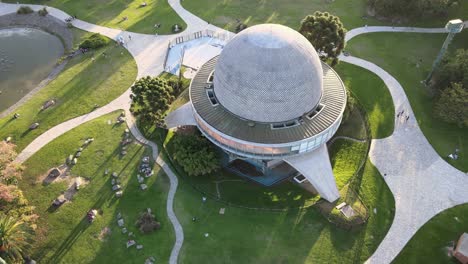 Aerial-lowering-on-Galileo-Galilei-Planetarium-between-paths-in-Palermo-Woods-at-golden-hour,-Buenos-Aires