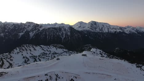 Chamrousse-ski-resort-in-the-French-Alps-during-sunrise-with-tracks-below,-Aerial-pan-left-reveal-shot