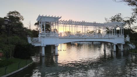 Aerial-panning-of-white-bridge-over-pond-at-Rosedal-gardens-in-Palermo-neighborhood-at-sunset,-Buenos-Aires