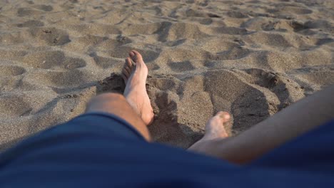 Male-pushing-sand-with-feet-lying-on-sandy-beach,-low-point-of-view-of-feet