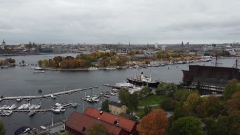aerial-view-moving-away-from-the-vasa-museum-in-stockholm,-sweden,-you-can-see-the-island-Djurgarden,-in-the-background-the-city-with-its-canals