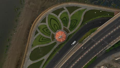 Park-designed-with-Lotus-flower-pattern,-Saigon-River,-traffic-bridge,-canal-and-main-road-rotating-counter-clockwise-from-a-top-down-drone-shot