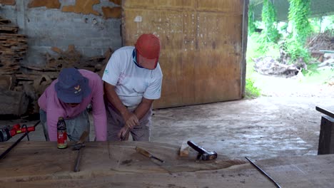 Two-carpenter-workshop-workers-renovate-old-wooden-table-top,-use-manual-jack