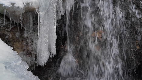 Spring-meltwater-cascading-over-frozen-waterfall,-winter-mountain-stream-closeup