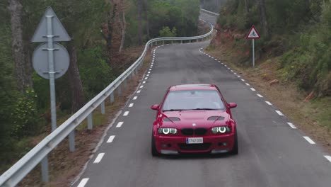 Ominoso-Automóvil-Bmw-Rojo-De-Lujo-Conduciendo-Hacia-La-Cámara-En-La-Sinuosa-Carretera-Rural-De-Barcelona