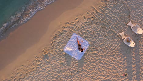 Einsame-Junge-Frau-Im-Bikini,-Die-Bei-Sonnenuntergang-Mit-Einer-Flasche-Wein-Am-Strand-Liegt