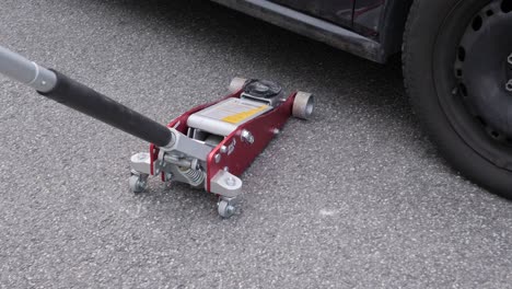 Positioning-a-red-hydraulic-car-jack-under-a-black-auto-to-change-tires
