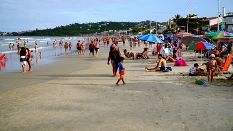 Dolly-in-of-people-sitting-by-the-shore-and-walking-by-the-sea-at-Bombas-and-Bombinhas-beaches,-Brazil