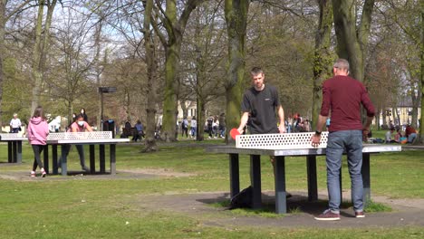 People-play-table-tennis-in-the-afternoon-sun-on-Christs-Pieces-in-Cambridge,-Cambridgeshire,-UK