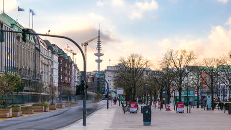 Toma-De-Lapso-De-Tiempo-Del-Paseo-Urbano-De-Jungfernstieg-Con-Tráfico-Y-Peatones-Durante-La-Puesta-De-Sol-Y-La-Torre-De-Televisión-En-Segundo-Plano