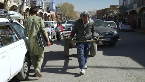 Hombre-Local-Tirando-De-Un-Carro-De-Madera-En-La-Carretera-Con-Personas-Y-Vehículos-En-Bamyan,-Afganistán