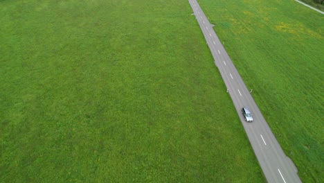 Lonely-car-drives-on-a-straight-street-in-a-green-meadow,-copy-space,-aerial
