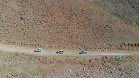 Aerial-View-Of-Trio-Of-Trucks-Riding-Along-Dirt-Road-On-Side-Of-Hill-In-Balochistan