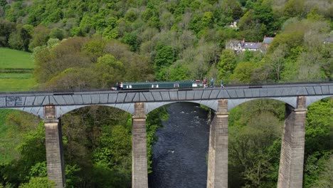 Aerial-view-following-narrow-boat-on-Trevor-basin-Pontcysyllte-aqueduct-crossing-in-Welsh-valley-countryside-zoom-in