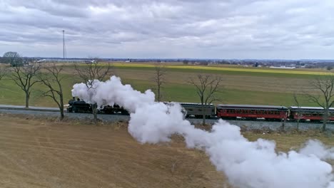 An-Aerial-View-of-a-Steam-Train-With-a-Drone-Following-Along-Side-Blowing-Smoke-and-Steam-Traveling-Thru-the-Countryside-on-a-Winter-Day