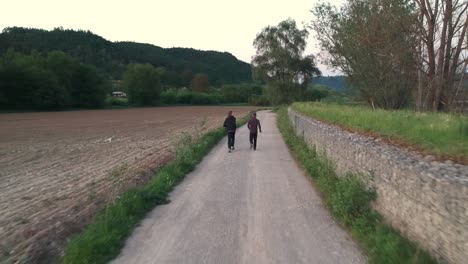 Dos-Personas-Corriendo-Por-La-Pista-De-Tierra-Del-Campo-Rural-En-La-Hora-Dorada-Al-Lado-Del-Campo