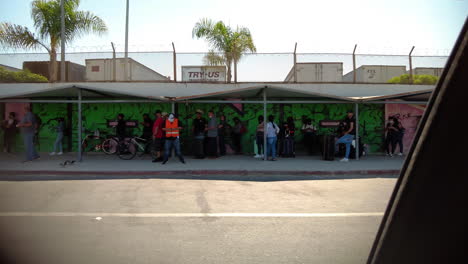 Vista-Desde-Un-Camión-En-Movimiento-De-Personas-Esperando-En-Fila-Para-Cruzar-La-Frontera-De-México-A-Estados-Unidos