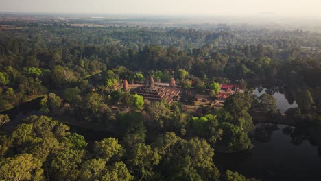 Angkorian-temple,-Bakong,-nested-in-the-mystic-Cambodian-jungle-and-early-morning-mist,-aerial-drone-footage