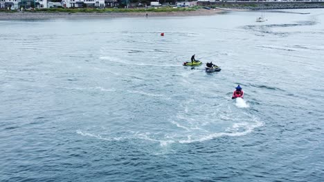 Gruppe-Auf-Jetskis,-Die-Auf-Dem-Fluss-In-Der-Nähe-Eines-Festgemachten-Segelboots-In-Der-Nähe-Der-Küstenstadt-Kreisen