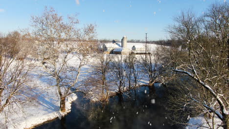 AERIAL-Snowing-Over-River-And-Rural-Farm-Property,-STATIC-SHOT
