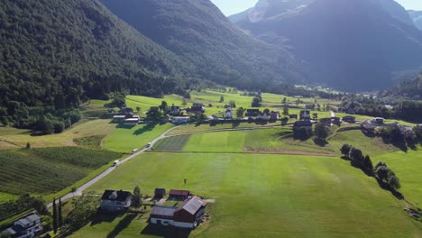 Green-farmland-fields-in-Lodalen-Nordfjord-Norway---Forward-moving-aerial-besides-road-fv723-and-against-Loen-church---Norway-aerial-in-beautiful-morning-light