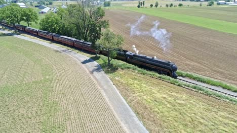 Eine-Drohnenansicht-Einer-Dampflokomotive-Mit-Personenwagen,-Die-Sich-An-Einem-Schönen-Sommertag-über-Die-Landschaft-Nähern