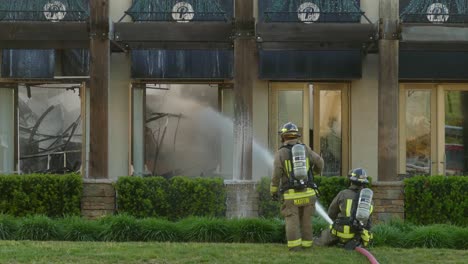 Pair-of-firefigthers-direct-the-water-jet-to-the-building-in-fire-wide-shot