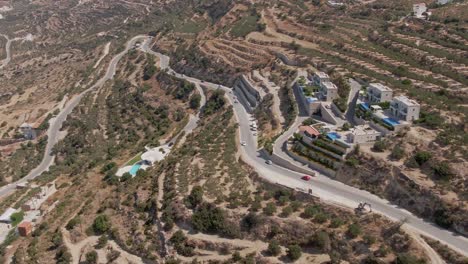 Curvy-road-with-many-vehicles-driving-in-hilly-area-of-Crete-island,-aerial-view