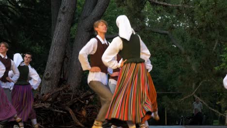 Adult-dancers-in-traditional-folk-costumes-perform-in-a-dance-performance-in-open-air,-sunny-summer-evening,-happy,-Latvian-national-culture,-medium-shot