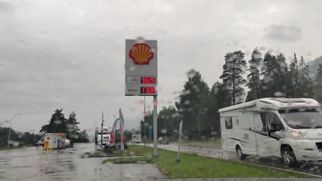 Frustración-Por-Los-Altos-Precios-Del-Combustible---Cartelera-Vista-Desde-El-Interior-Del-Coche-Con-Lluvia-En-La-Ventana-Delantera-Y-Tráfico-Que-Pasa---Clip-Estático-De-Día-Lluvioso-Con-Tráfico-Que-Pasa-Noruega