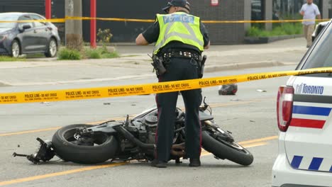 Escena-Del-Accidente-De-Moto-Cubierta-Con-Cinta-Amarilla-Mientras-El-Oficial-De-Policía-Revisa-La-Bicicleta