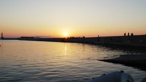 Beautiful-Sunset-view-over-Aegean-Sea-in-Chania,-tourists-Enjoying-old-venetian-harbor-with-historic-lighthouse-during-summer-evening,-Sightseeing-Spot-in-Greece