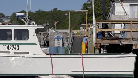 Pescadores-Comerciales-De-Langosta-Descargando-Su-Captura-Del-Día-En-Un-Pequeño-Puerto-En-La-Costa-De-Maine-Visto-Desde-Otro-Barco-En-El-Agua