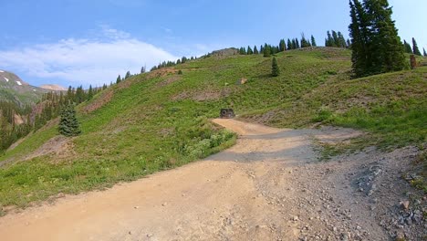 Pov-Siguiendo-Un-Jeep-Conduciendo-Por-Un-Sendero-Circular-Alpino-Cortado-En-La-Ladera,-A-Través-De-Un-Prado-En-Las-Montañas-San-Jan-Cerca-De-Silverton-Colorado