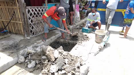 Foremen-wearing-safety-reflective-vests-use-their-shovel-and-demolition-hammer-to-perform-deep-excavation-beside-the-road-and-gutter-for-installing-new-water-piping-from-the-main-water-line