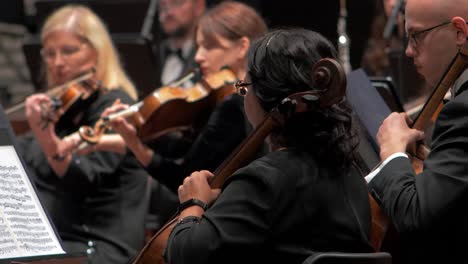 Konzentrieren-Sie-Sich-Auf-Eine-Musikerin,-Die-Mit-Einem-Orchester-Geige-Spielt,-Liepāja-Symphonieorchester-Saisoneröffnungskonzert,-Konzertsaal-Großer-Bernstein,-Mittlere-Aufnahme,-Regal-Fokus-Auf-Cellospieler