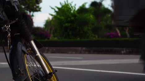 Static-view-from-ground-level-of-traffic-crossing-road-with-focus-on-motorcycle-wheel